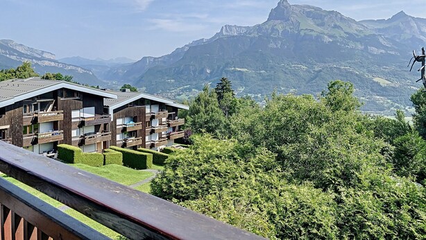 Un chalet de montagne doté de plusieurs balcons offrant une vue sur une vallée et des montagnes.