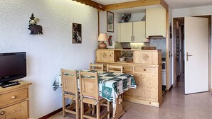 Une cuisine de taille réduite avec des meubles de rangement en bois, une table à manger avec des chaises et un téléviseur posé sur un meuble en bois.
