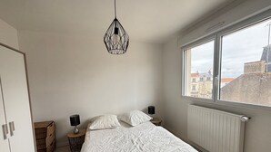 A bedroom with a bed, a window, a radiator, and a hanging light fixture. - Charming City Center House with Beach Access, Free WiFi, Garage, Baby Gear, & Renovated Interiors (Les Sables-d'Olonne)