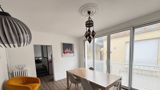 A dining area with a wooden table and chairs, a yellow armchair, and a large window with a view of the outside. - Charming City Center House with Beach Access, Free WiFi, Garage, Baby Gear, & Renovated Interiors (Les Sables-d'Olonne)