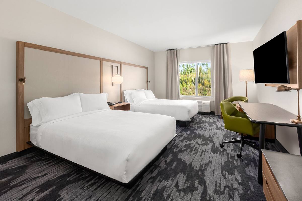 Une chambre d’hôtel avec deux lits, un bureau, une chaise, une télévision et une fenêtre avec des rideaux.