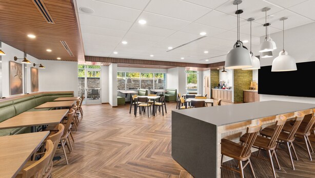 A modern restaurant with wooden flooring, green booths, and a central bar area.