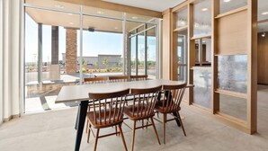 A modern dining area with a large table and chairs, large windows with a view of the outside, and a stone pillar.
