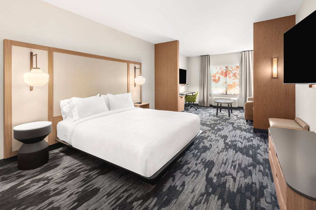 Une chambre d’hôtel avec un grand lit, un bureau, une chaise, une télévision et une fenêtre avec des rideaux.