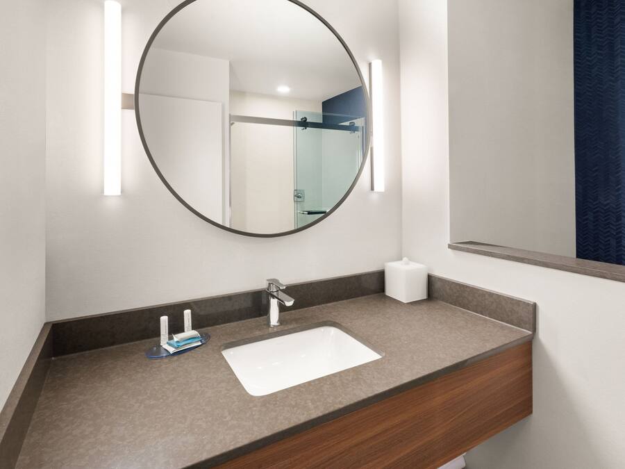 A modern bathroom with a round mirror, a white sink, and a towel dispenser.