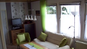 En stue med sofa, to lænestole, sofabord, tv på et skab og en gulvlampe.