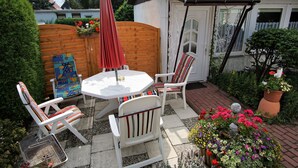 En terrasse med et rundt bord og fire stole, et træhegn og en potteplante med blomster.