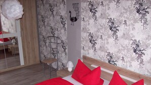 Et soveværelse med seng, røde puder, et natbord, en lampe og et spejl.