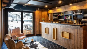 Eine Bar mit Holzwänden, einem sechseckigen Fliesenboden, Ledersesseln und Blick auf eine verschneite Landschaft.