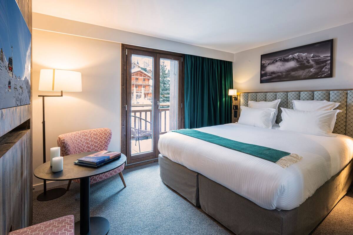 Habitación de hotel con una cama grande, un escritorio, una silla, una lámpara y vistas a un edificio a través de la ventana.