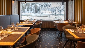 Ein Restaurant mit gedeckten Tischen, Blick auf eine verschneite Landschaft durch große Fenster und einem modernen Interieur.