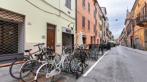 A street with bicycles parked on a rack, buildings with signs, and a clear sky. - GuestHost - Ferrara Torre dei Leuti White Apartment (Ferrara)