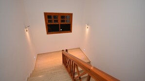 Un escalier en bois avec une rampe, une petite fenêtre à cadre en bois et deux lampes fixées au mur.