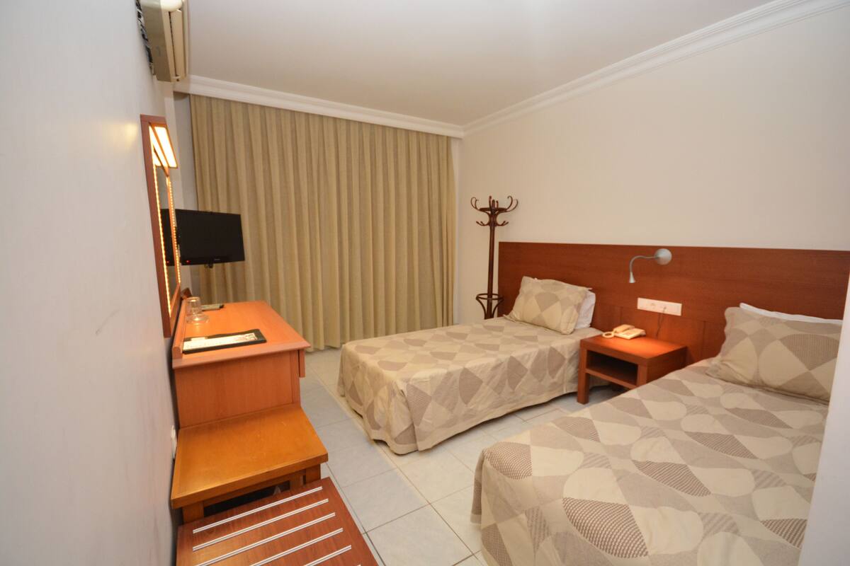 Habitación de hotel con dos camas, un escritorio con lámpara, un perchero y un televisor.