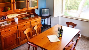 Un comedor con una mesa de madera, sillas, un televisor y una ventana con vista a follaje.
