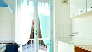 Una cocina con encimera blanca, un lavabo y una puerta con cortinas.