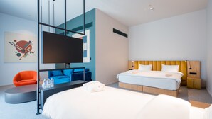 A modern hotel room with a large bed, a desk, a chair, and a TV.