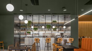 A modern bar with wooden chairs and tables, a bar counter with shelves of bottles, and hanging lights. - Episode Tbilisi (Tbilisi)