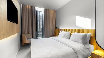 Habitación de hotel moderna con una cama grande, un televisor de pantalla plana montado en la pared, un sillón cómodo y vistas a la ciudad desde la ventana.