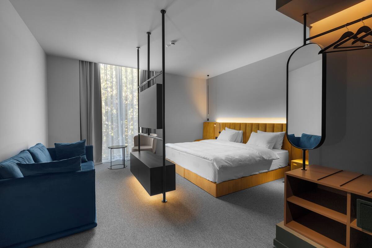 A modern hotel room with a bed, a sofa, a desk, and a mirror.