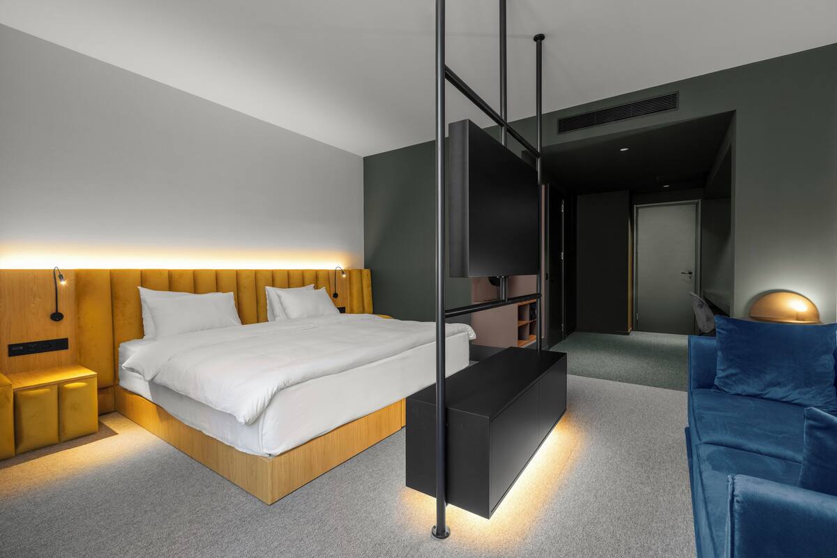 A modern hotel room with a bed, a TV, a sofa, and a desk.