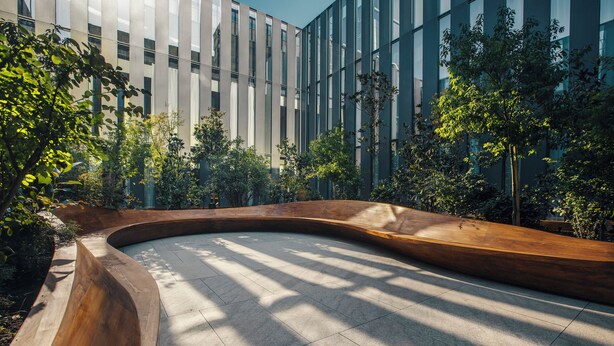 A modern building with a curved wooden bench and surrounding greenery.