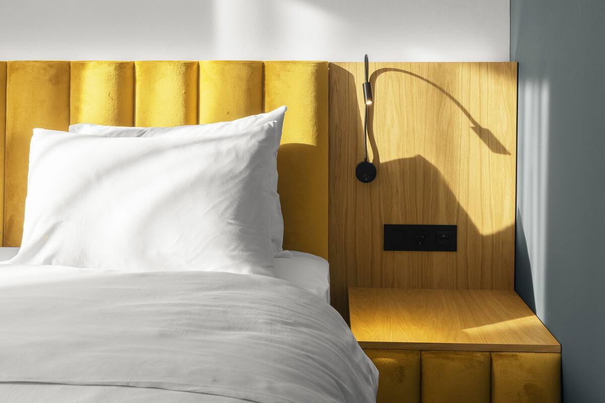 A modern bedroom with a bed, a wooden nightstand, and a wall-mounted lamp.