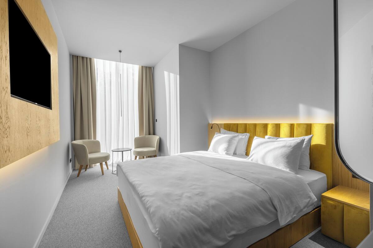 A modern hotel room with a large bed, a seating area with two chairs, a small table, and a TV mounted on the wall.