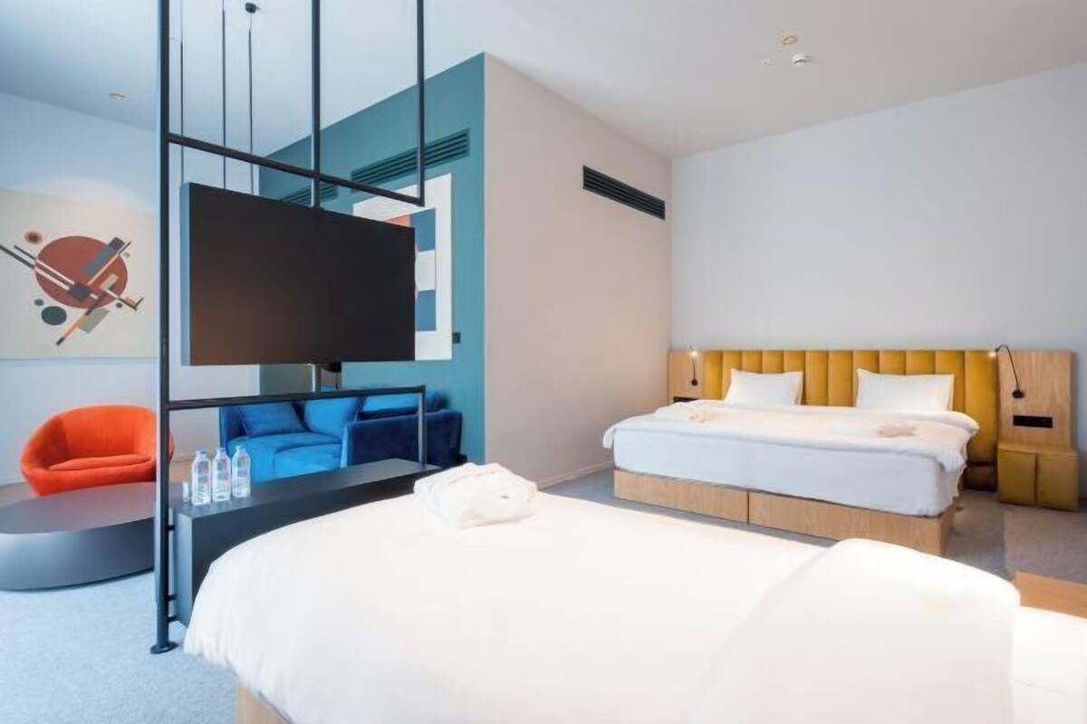 A modern hotel room with a bed, a TV, a desk, and a chair.