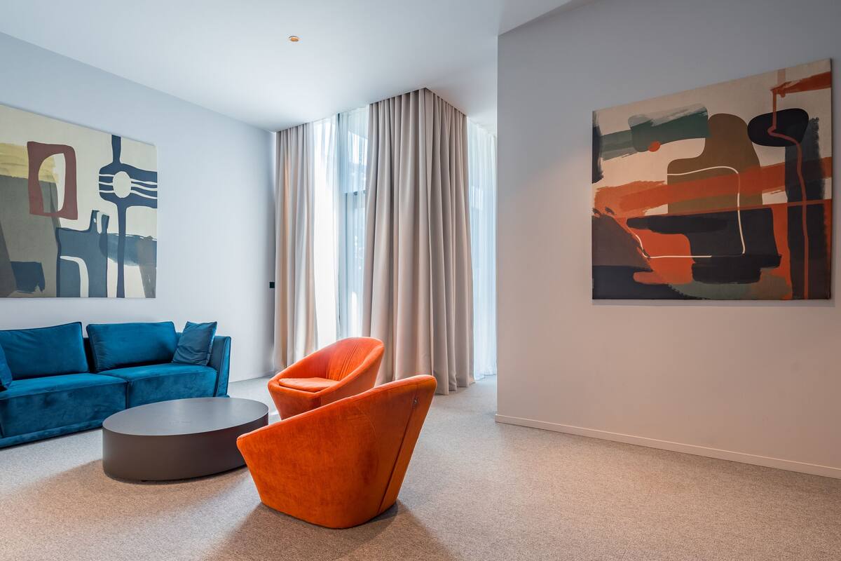A modern living room with a blue sofa, an orange armchair, and two abstract paintings on the walls.