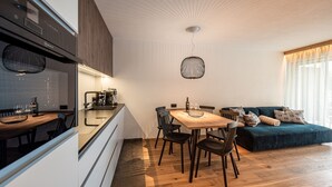 Eine moderne Küche mit Einbauherd, ein Essbereich mit Holztisch und -stühlen sowie eine gemütliche Sitzecke mit blauem Sofa und gemusterten Kissen.