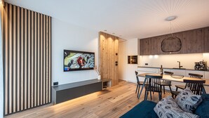 Eine moderne Küche mit einer Holzwand, einem Essbereich mit einem dunkelblauen Sofa und einem an der Wand montierten Fernseher.