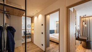 Ein modernes Hotelzimmer mit Holzboden, einem Bett mit blauer Kopfteil, einem kleinen Tisch mit Stuhl und einem Badezimmer mit Spiegel und Waschbecken.