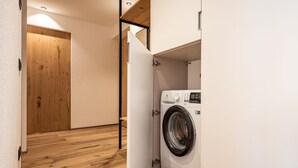 Ein Waschraum mit einer Waschmaschine mit Frontlader, Holzboden und einer Tür zu einem anderen Raum.