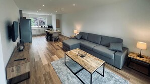 A modern living room with a grey sofa, a wooden coffee table, and a TV mounted on the wall. - 3-room gîte with terrace (Wintzenheim)