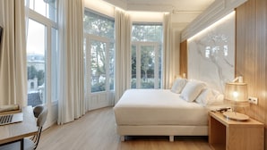 A bedroom with a large bed, a desk with a laptop, and a nightstand with a lamp.