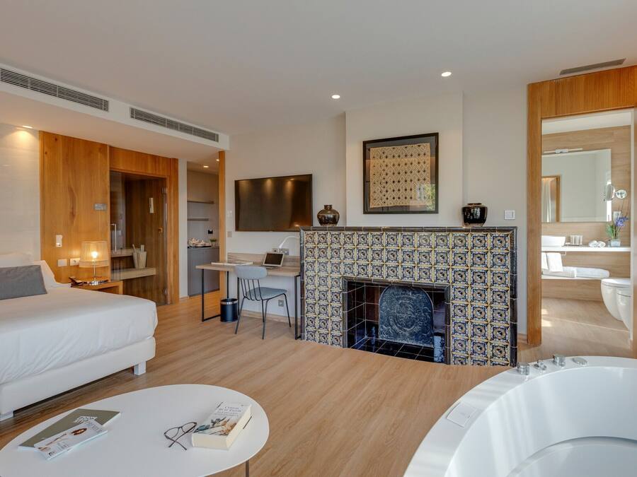 Una habitación de hotel moderna con cama, escritorio, chimenea, baño y bañera de hidromasaje.