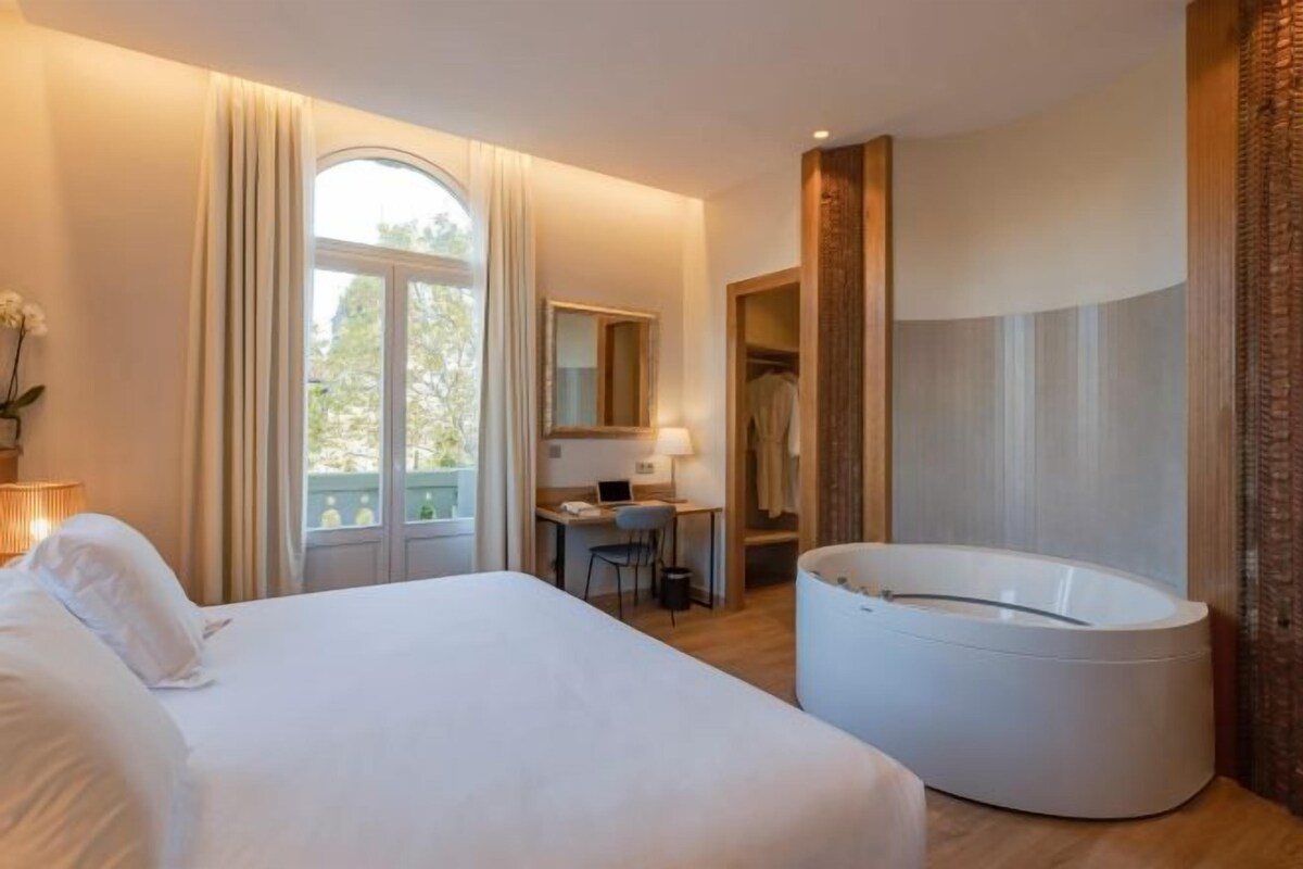 Un dormitorio con cama, escritorio, silla, bañera y ventana.