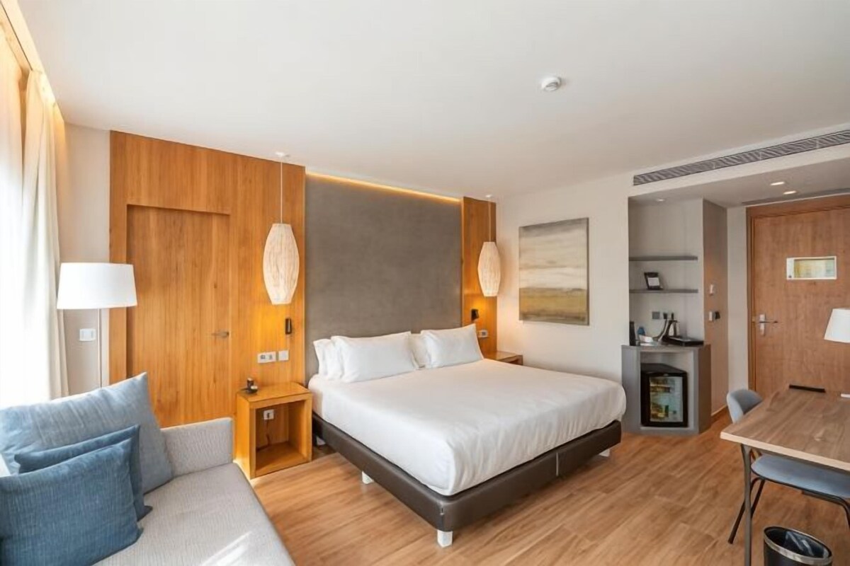 Una habitación de hotel moderna con una cama grande, mesitas de noche, un escritorio y una silla.