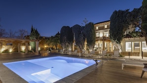 A swimming pool with a wooden deck, surrounded by lounge chairs and a building with multiple windows.
