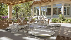 An outdoor dining area with tables set for a meal, surrounded by wicker chairs and a pergola.