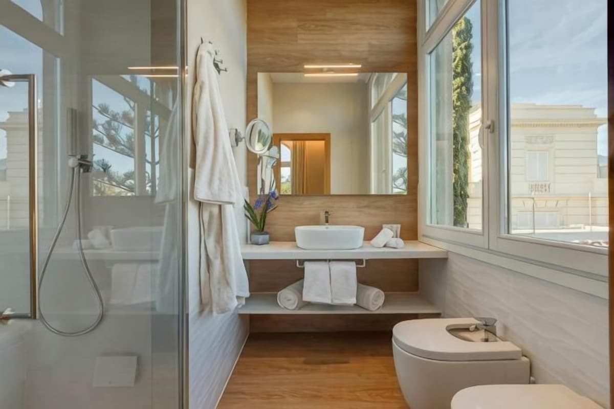 Un baño moderno con cabina de ducha de vidrio, tocador de madera, inodoro y ventana grande con vistas al exterior.