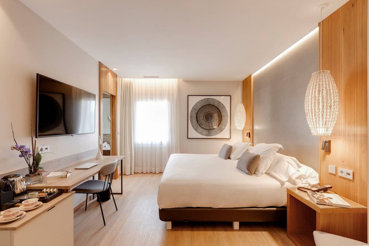 A modern hotel room with a large bed, a desk, and a TV.