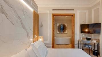 Une chambre d’hôtel moderne dotée d’un grand lit, d’un bureau avec un ordinateur portable, d’une télévision et d’une salle de bain avec baignoire.