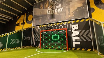 An indoor football field with artificial turf, goalposts, and a large wall with "ACTION FACTORY FOOTBALL" text.