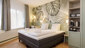 Een moderne hotelkamer met een groot bed, een houten hoofdbord, een nachtkastje, een lamp, een plank met toiletartikelen en een raam met gordijnen.