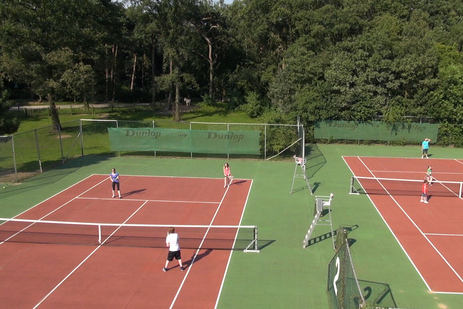 En tennisbane med flere baner, et net og et hegn.