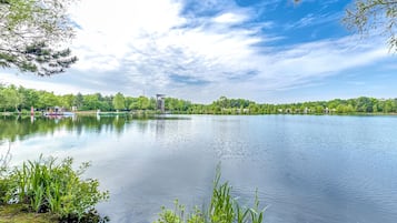 Un lago tranquillo con barche, un faro e una fila di case lungo la riva.