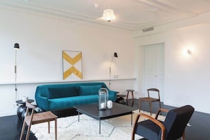 A modern living room with a teal sofa, a black coffee table, and a white shag rug.