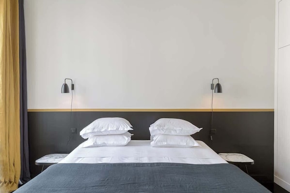 A hotel room with a bed, two bedside tables, and two wall-mounted lamps.